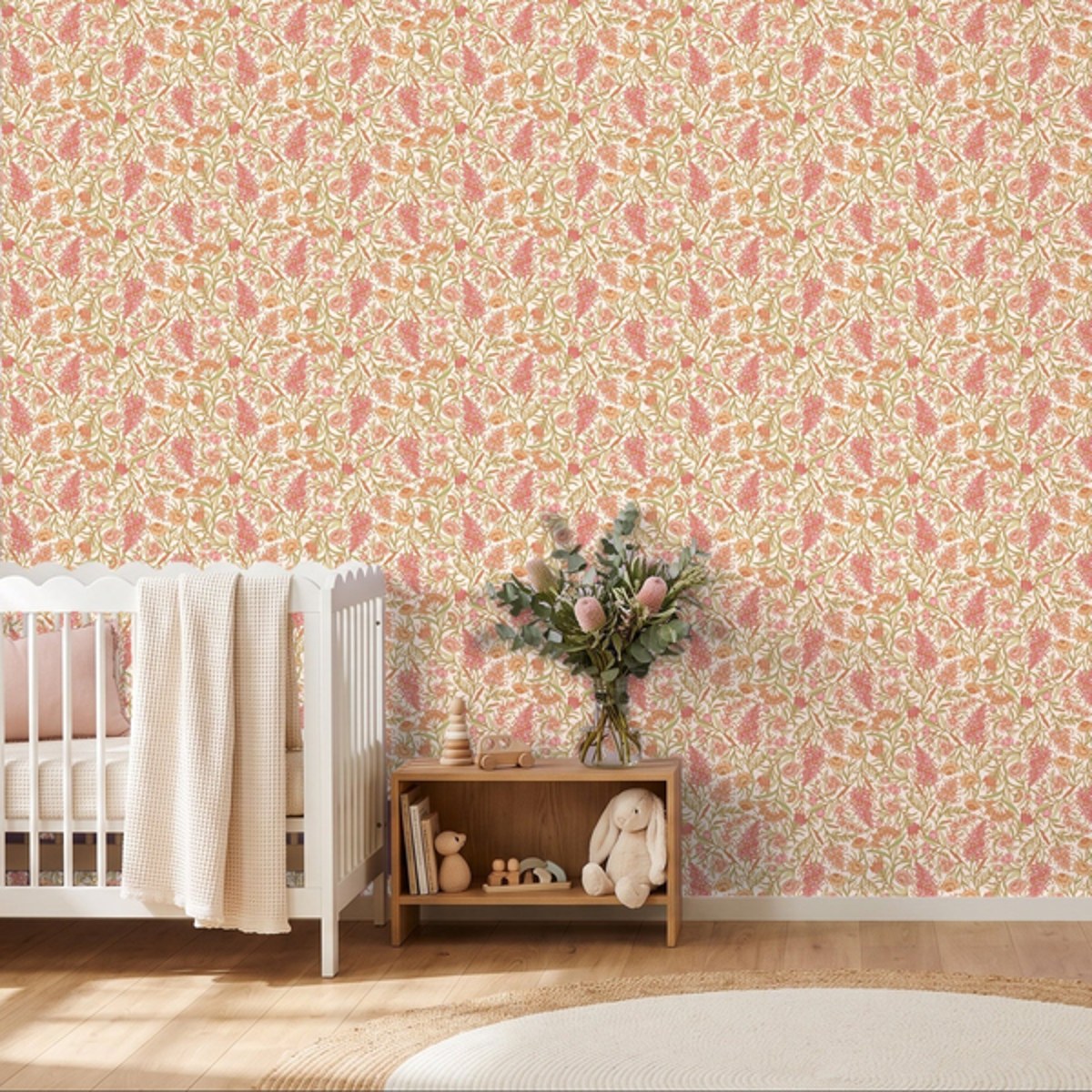 A nursery room featuring a pink and yellow floral patterned wallpaper on the wall, styled with a white crib, a wooden side table with flowers, a white dresser, and a round rug on a light wood floor.