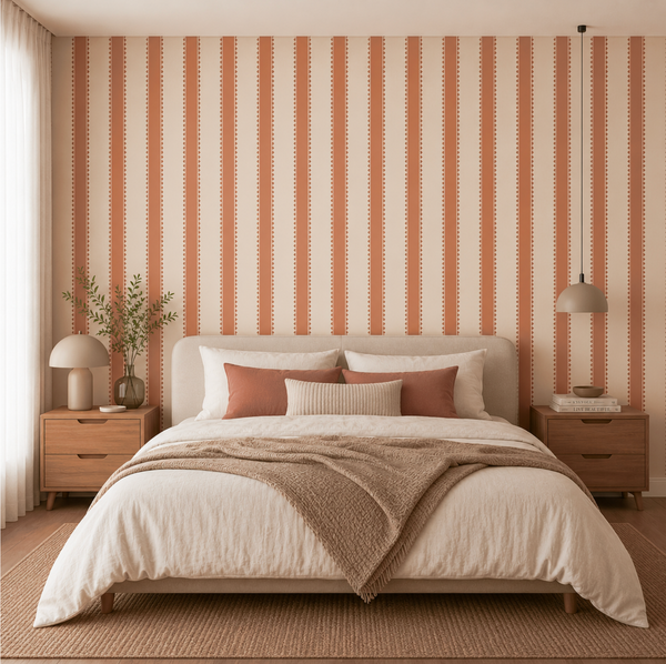 A styled bedroom featuring a bed with cream bedding and rust-colored pillows, set against a wall with vertical rust and cream stripes. The room includes matching wood nightstands, a table lamp, a hanging pendant light, and a textured rug.