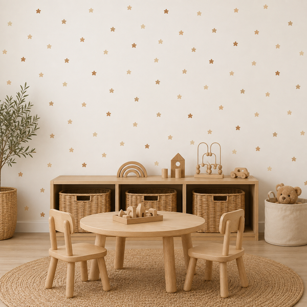 A styled children's playroom corner featuring a light natural wood round table and two matching chairs on a woven rug, set against a cream wall with gold star decals and a wooden storage cabinet with wicker baskets.