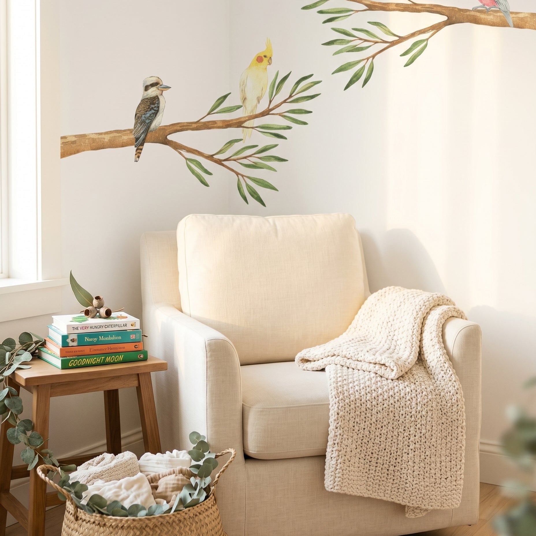 Beige armchair with a blanket, small table with books, and wall decal of birds on branches in a cozy room.