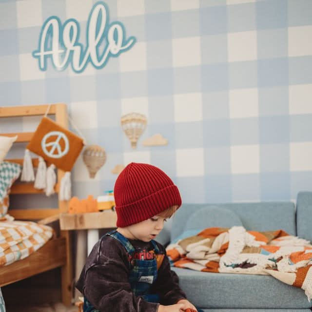 Child playing with building blocks on a checkered floor with a colorful wall in the background.

