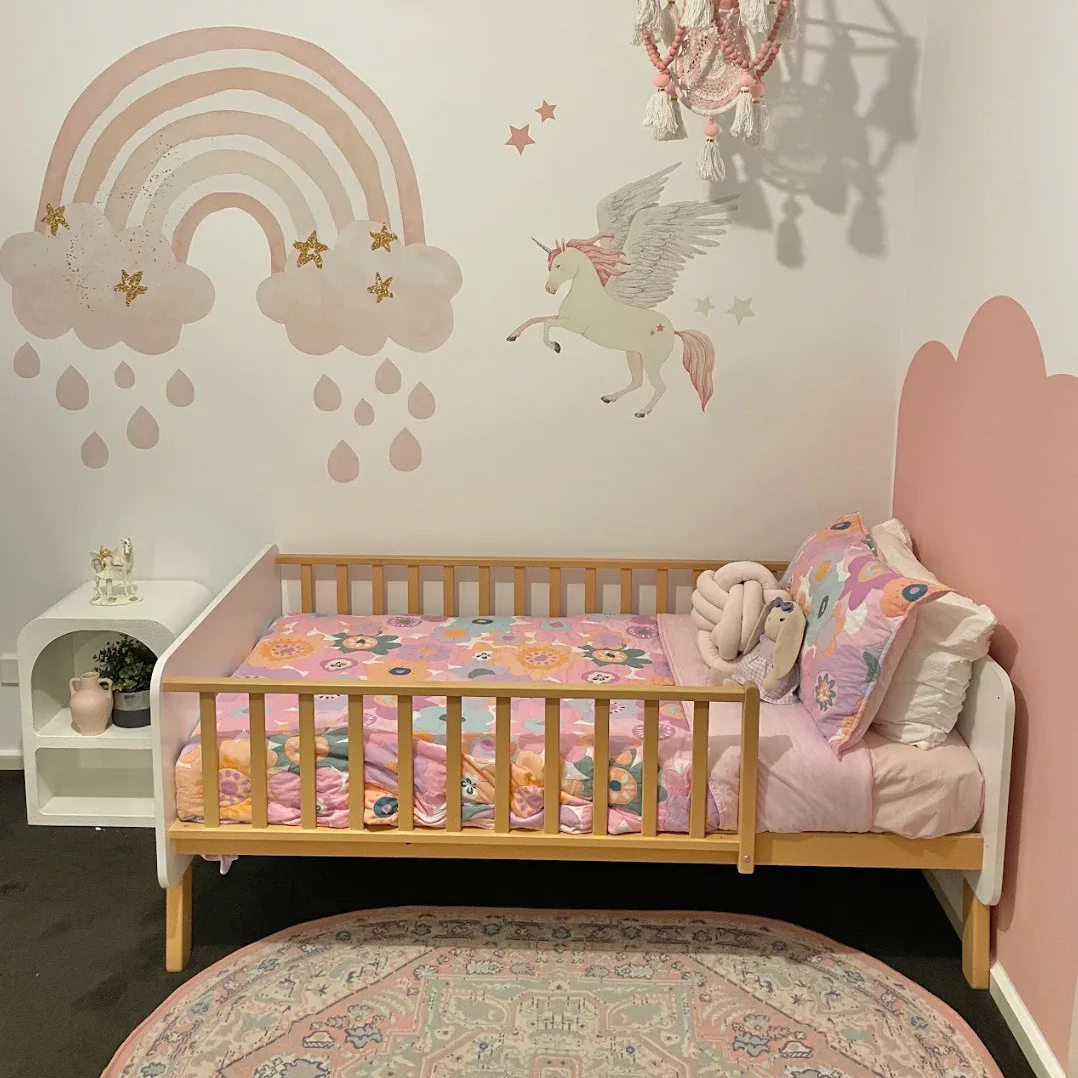 Children's bedroom with a bed, rainbow, and unicorn wall decals.