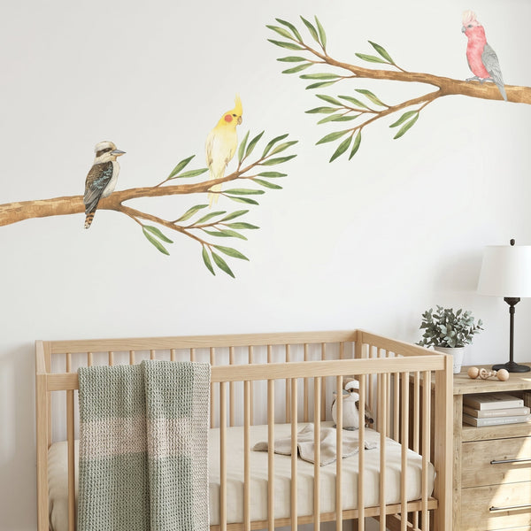 Nursery room with wooden crib, decorative wall stickers of birds on branches, and a dresser.