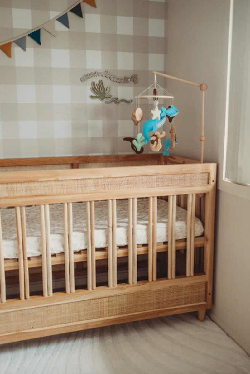 Corner of a nursery papered in Jumbo Traditional Gingham Wheat with a timber cot