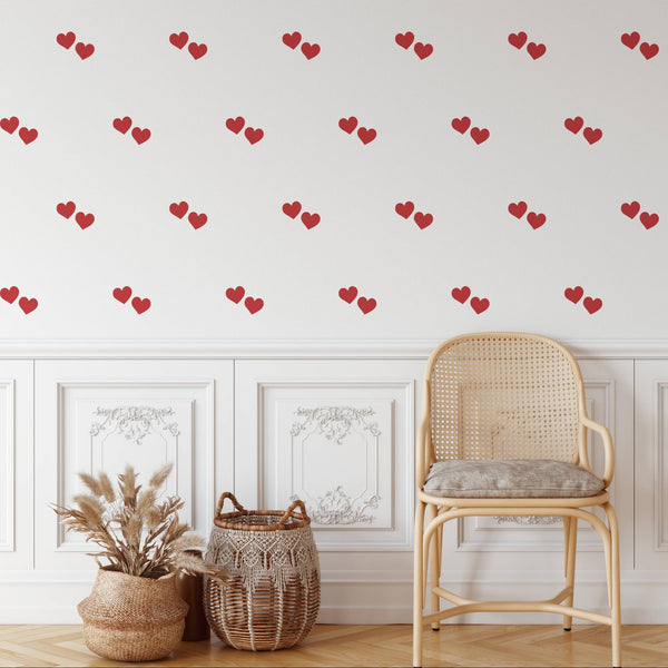 Wall with red heart wall decal pattern, chair, and decor items on a light wooden floor.