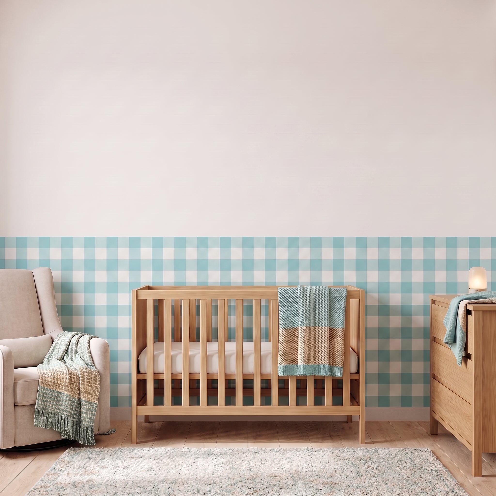 A styled nursery with aqua gingham check wallpaper across the lower half of the wall. The room has a light wood crib with white bedding and an aqua and tan blanket, a cream armchair with a woven throw, a matching wood dresser with a lamp, and a soft rug on a light wood floor.