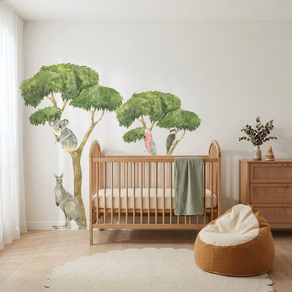 Hand-painted gum tree wall decals with a koala, galah, kookaburra and kangaroo beside an oak cot in a nursery