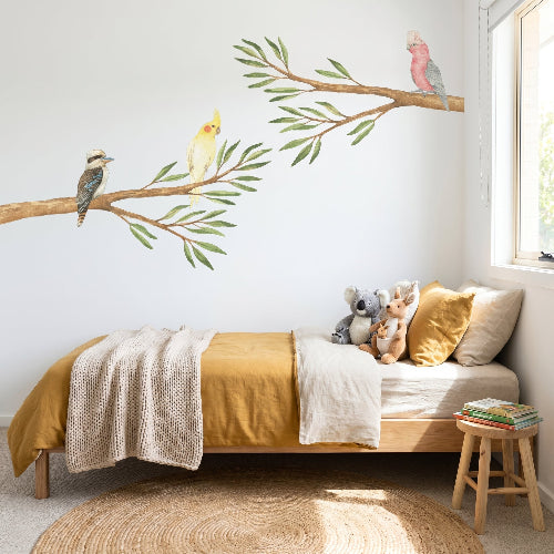 Children's bedroom with a bed, stuffed animals, and wall decals of birds and branches.