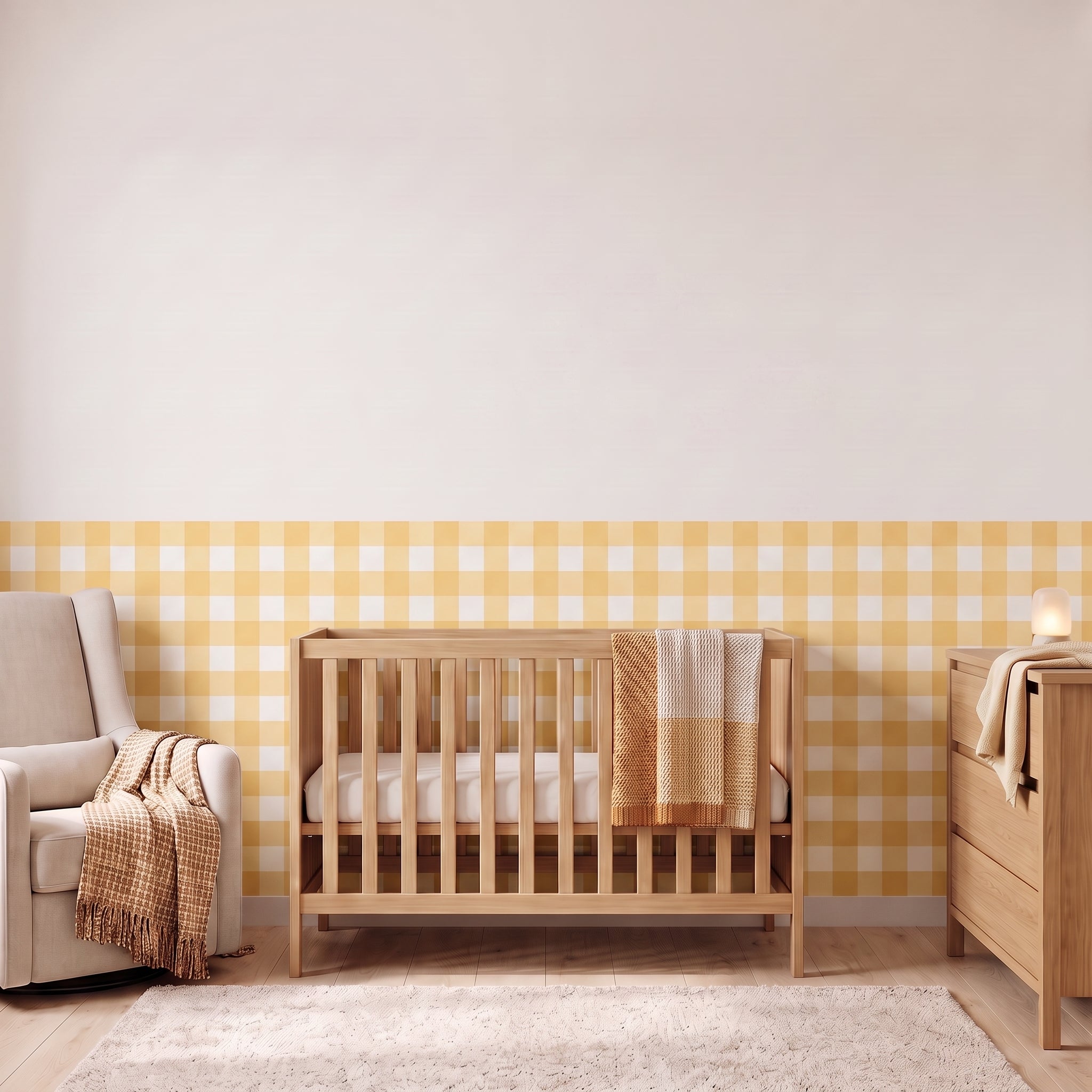 A styled nursery with buttercream yellow gingham check wallpaper across the lower half of the wall. The room has a light wood crib with white bedding and a buttercream and cream checked blanket, a cream armchair with a buttercream and cream fringed throw, a matching light wood dresser with a lamp, and a soft cream rug on a light wood floor.