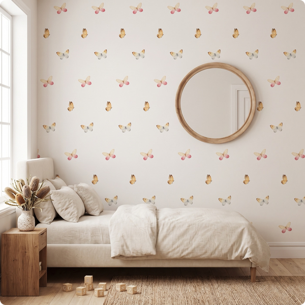 A styled children's bedroom featuring wallpaper with a repeating pattern of small butterflies and cherries in soft pastel colors. The room includes a single bed with cream bedding, a round wooden-framed mirror on the wall, a wooden side table with dried flowers, and a light wood floor.