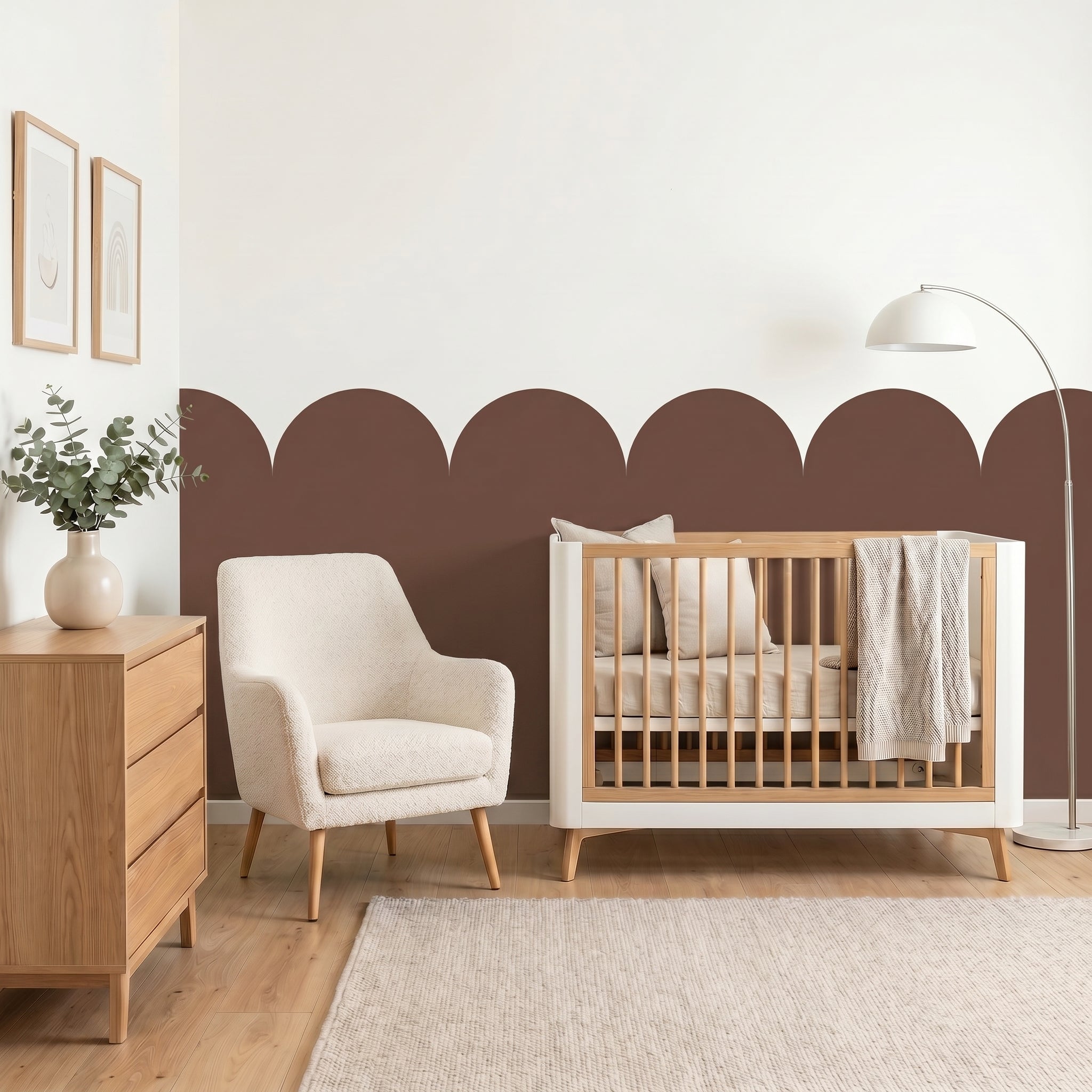 Nursery room with wooden crib, armchair, and dresser against a white wall with decorative brown arches.