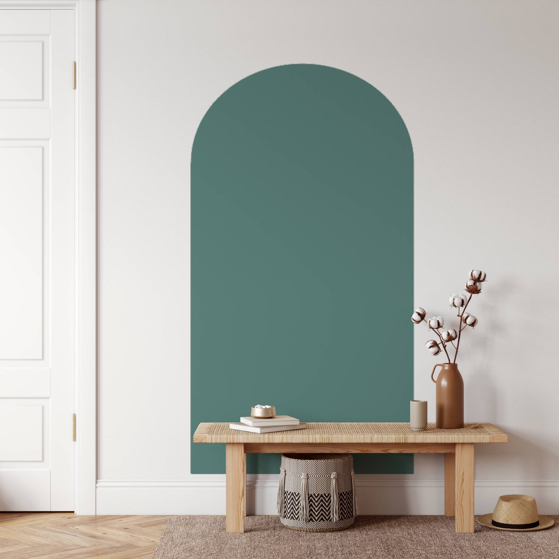 Teal arched mirror on a white wall with a wooden bench and decorative items.