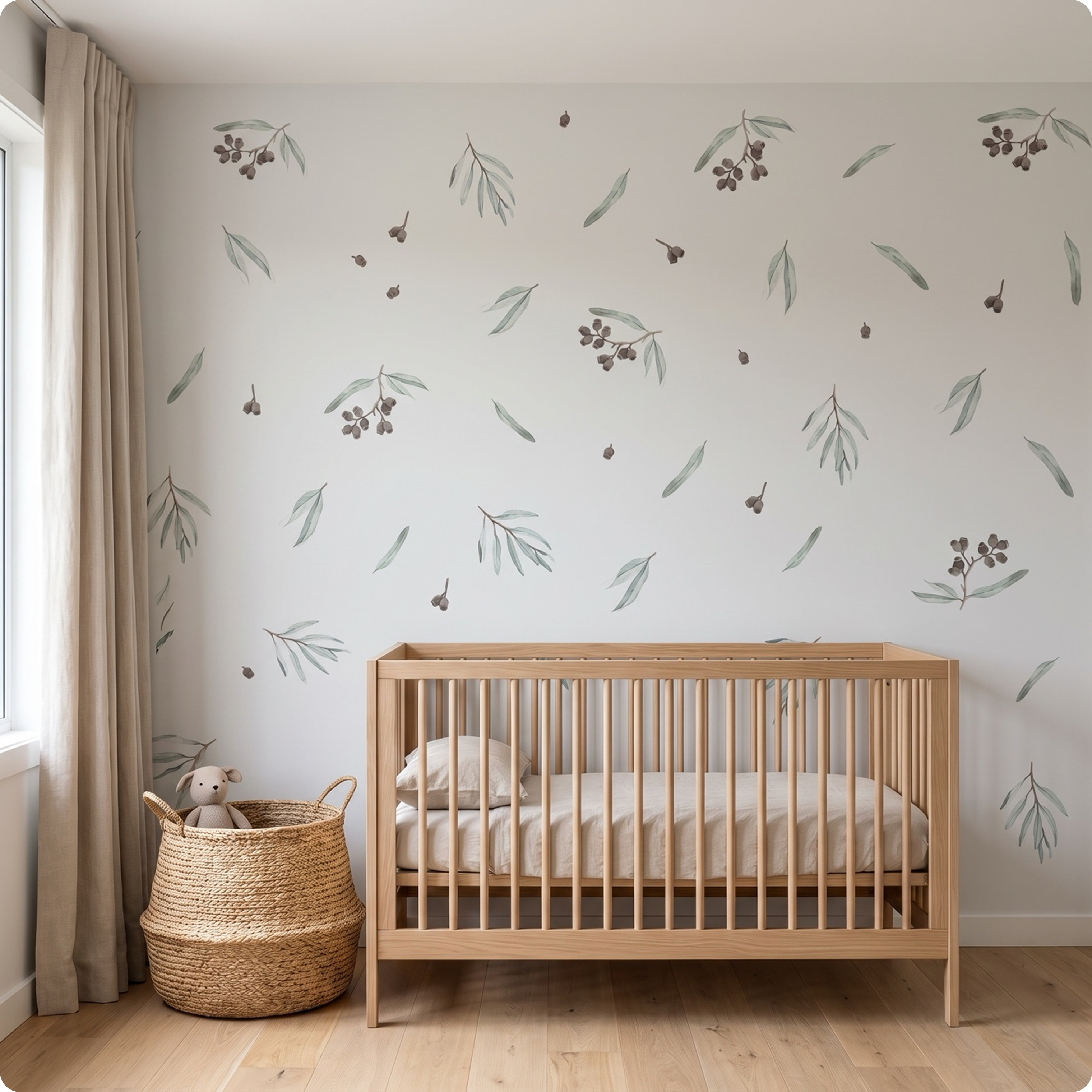 A light wood crib with a beige mattress in a nursery setting, set against a white wall decorated with watercolor-style olive branch decals. A woven basket with a plush toy sits on the wooden floor next to a beige curtain.