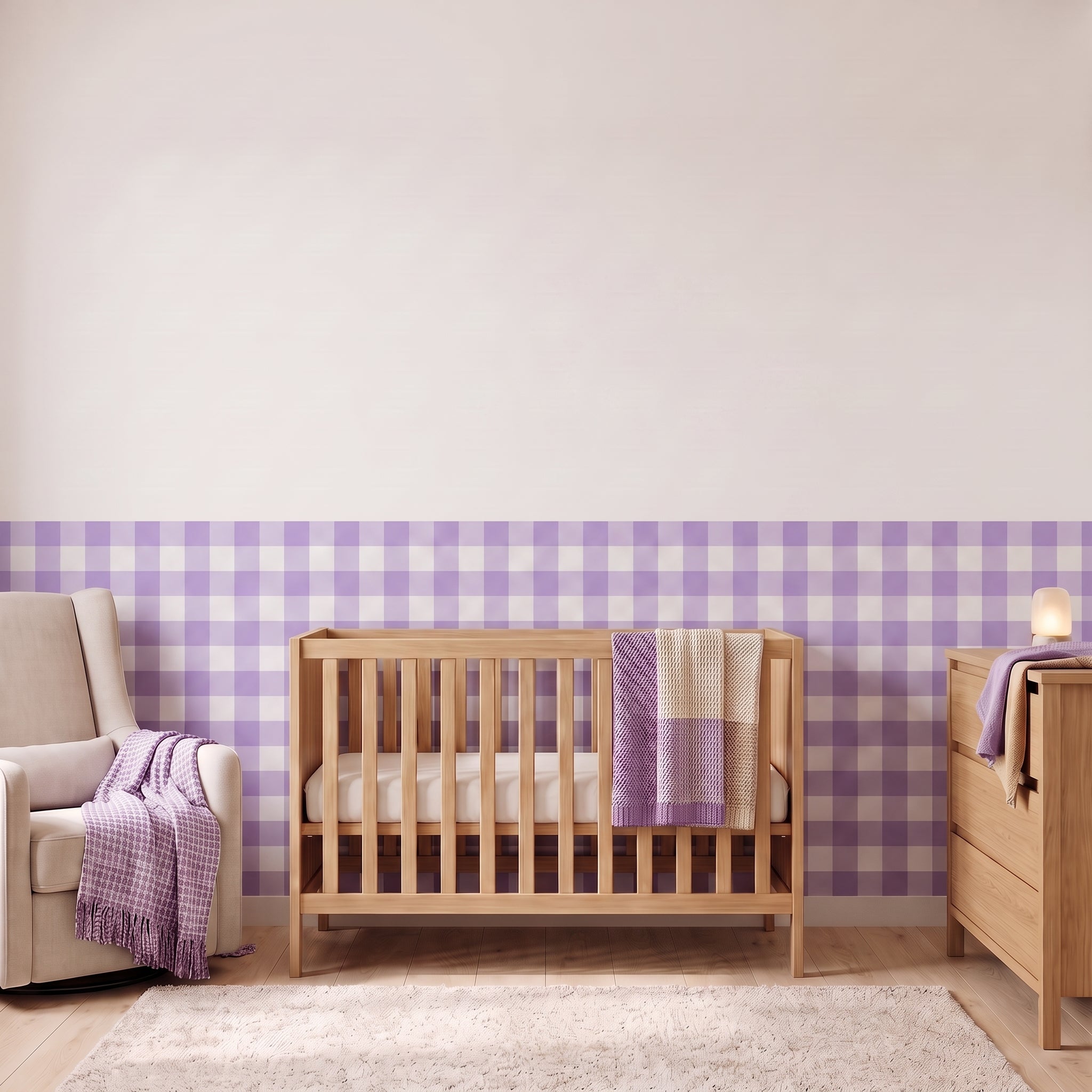 A styled nursery with lilac gingham check wallpaper across the lower half of the wall. The room has a light wood crib with white bedding and a lilac and cream blanket, a cream armchair with a lilac woven throw, a matching wood dresser with a lamp, and a soft rug on a light wood floor.