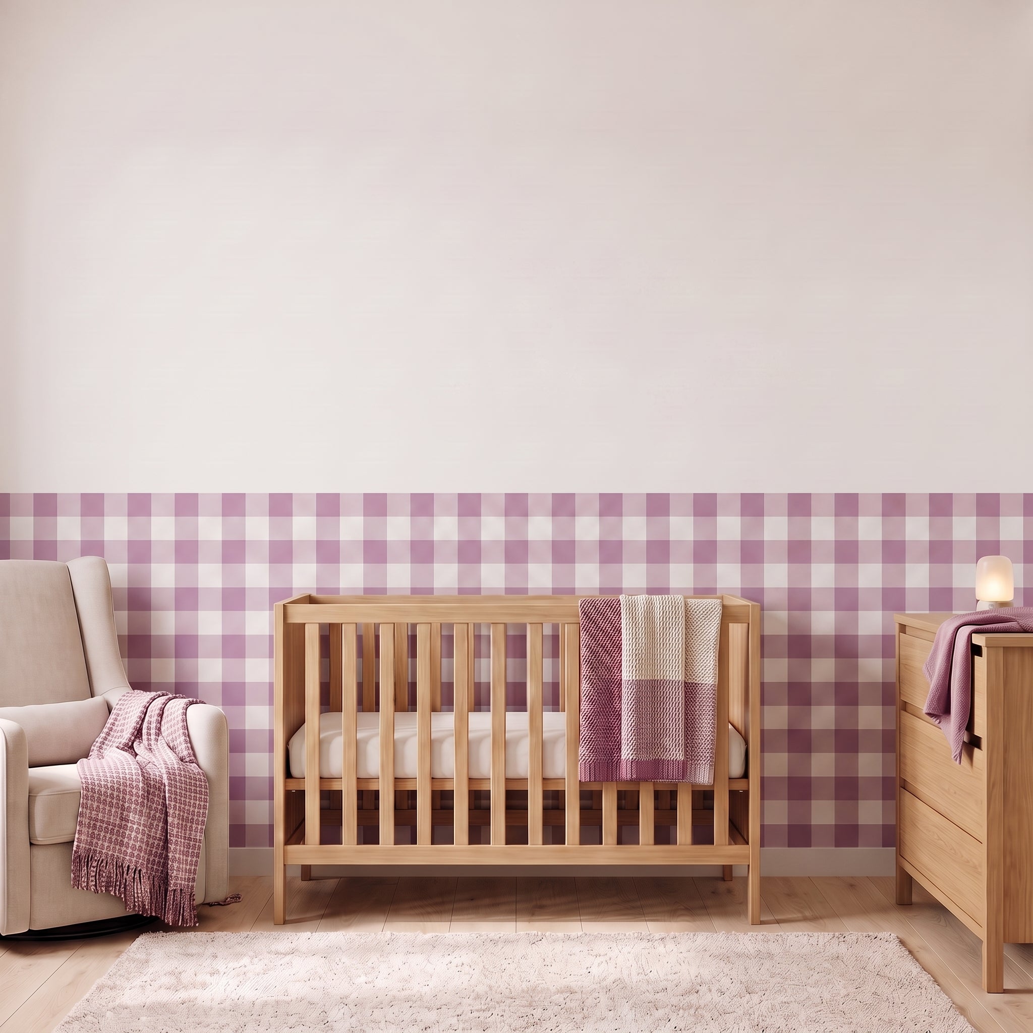 A styled nursery with orchid purple gingham check wallpaper across the lower half of the wall. The room has a light wood crib with white bedding and an orchid and cream blanket, a cream armchair with an orchid woven throw, a matching wood dresser with a lamp, and a soft rug on a light wood floor.