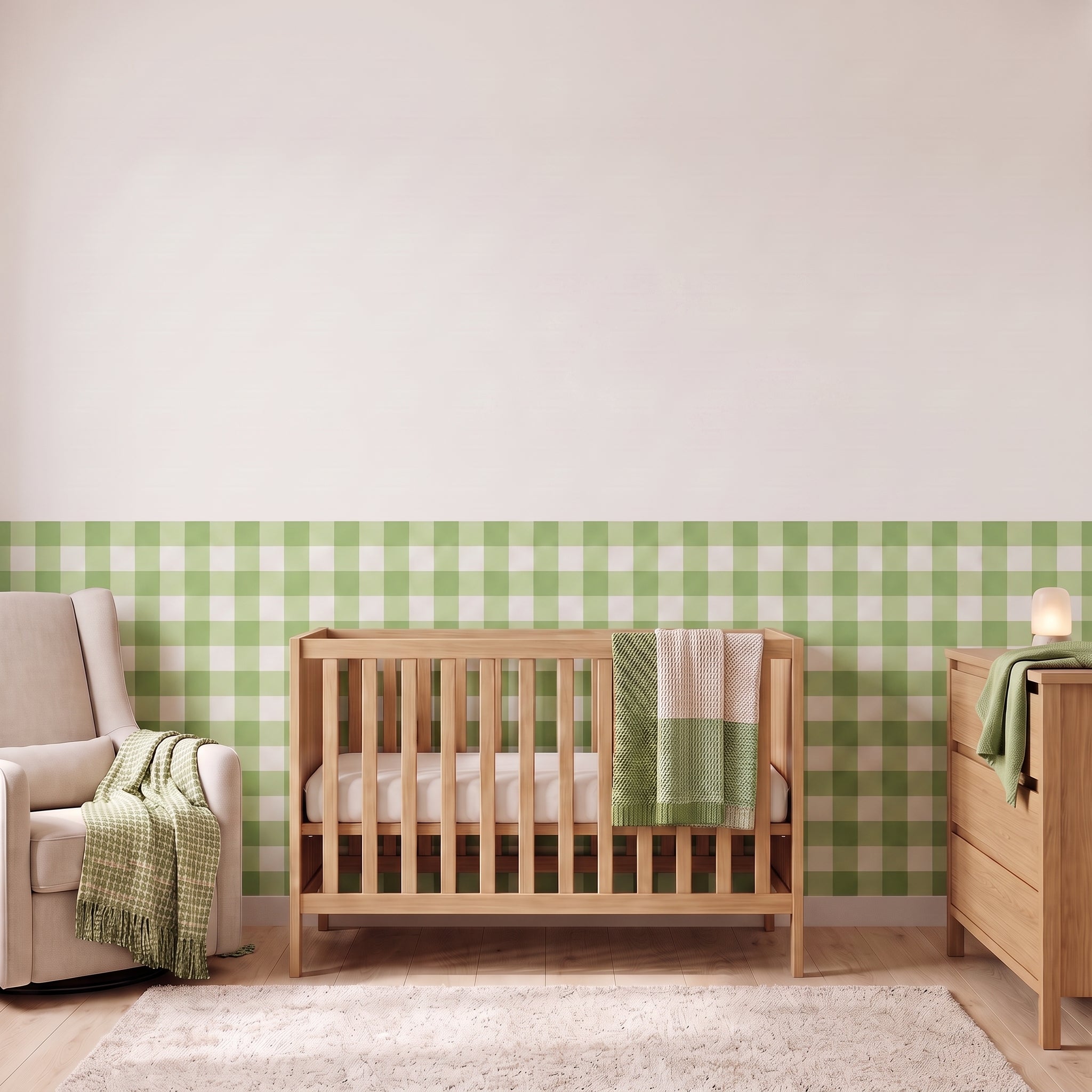 A styled nursery with pistachio green gingham check wallpaper across the lower half of the wall. The room has a light wood crib with white bedding and a pistachio green and cream checked blanket, a cream armchair with a green and cream fringed throw, a matching light wood dresser with a lamp, and a soft cream rug on a light wood floor.
