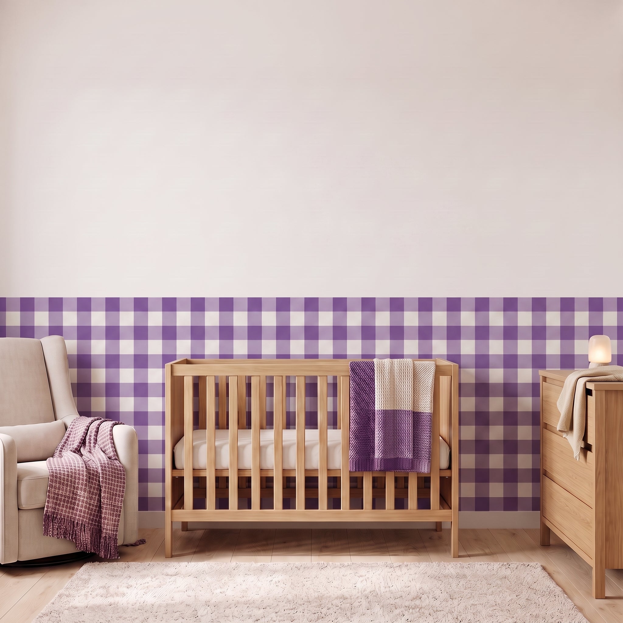 A styled nursery with plum purple gingham check wallpaper across the lower half of the wall. The room has a light wood crib with white bedding and a plum and cream blanket, a cream armchair with a plum woven throw, a matching wood dresser with a lamp, and a soft rug on a light wood floor.