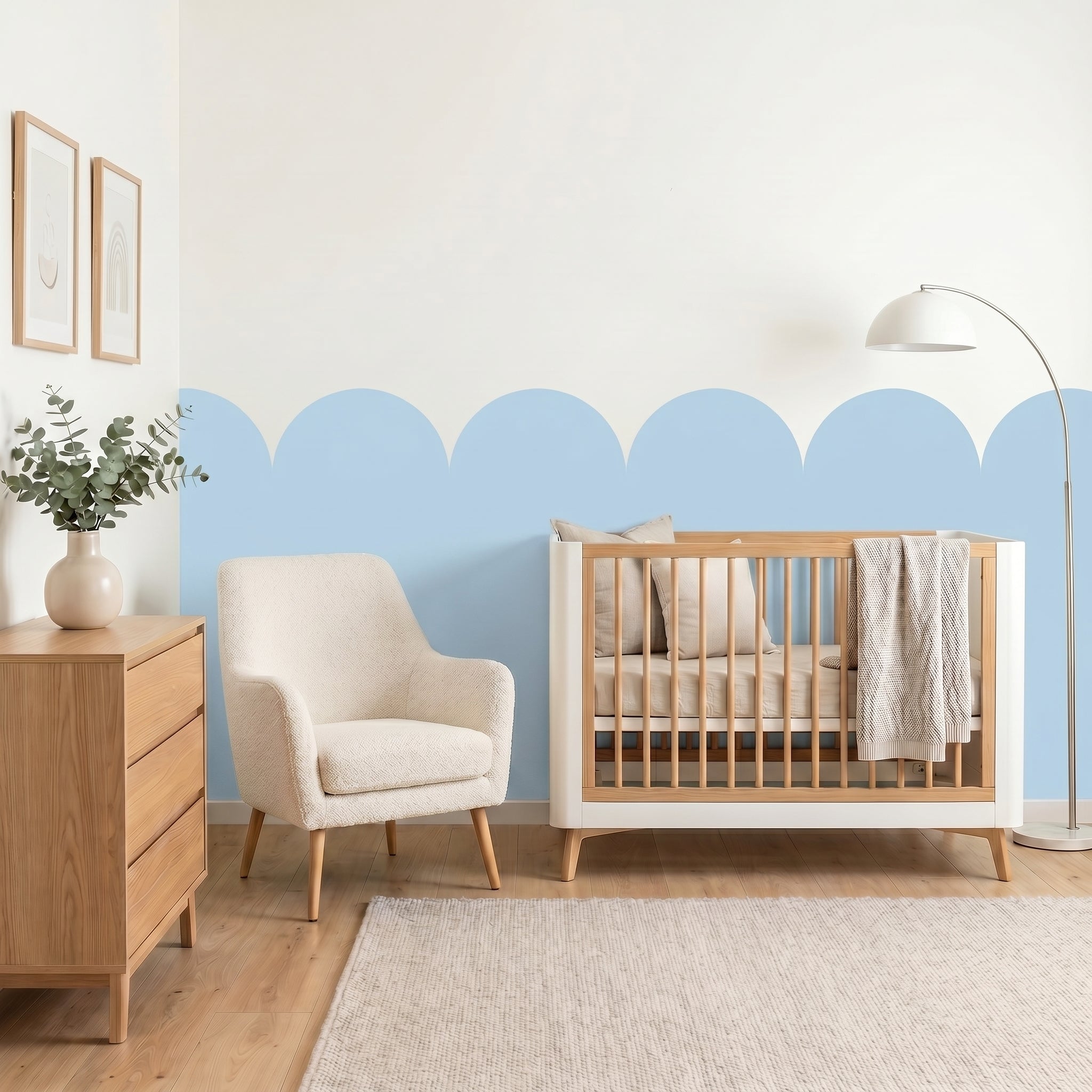 Nursery room with wooden crib, chair, and dresser against a light blue wall.