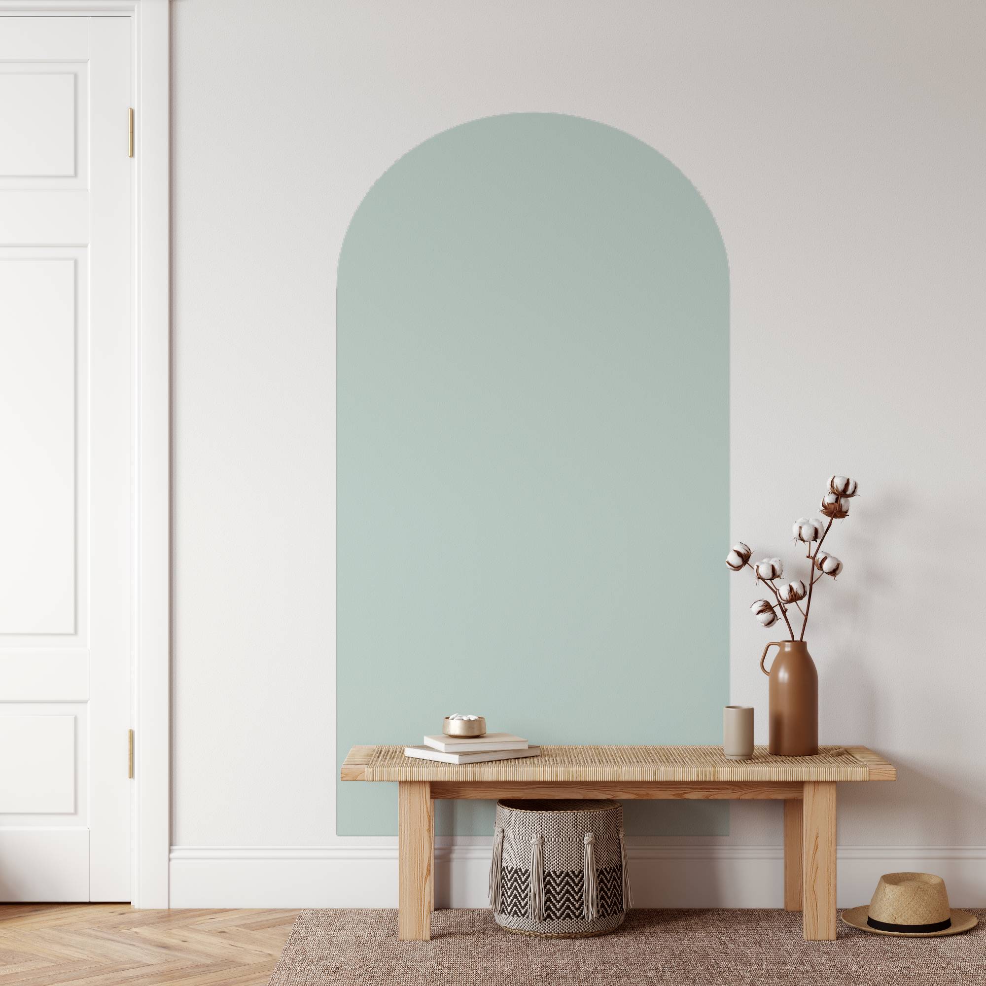 Arched mint green mirror on a white wall with a wooden bench and decorative items.