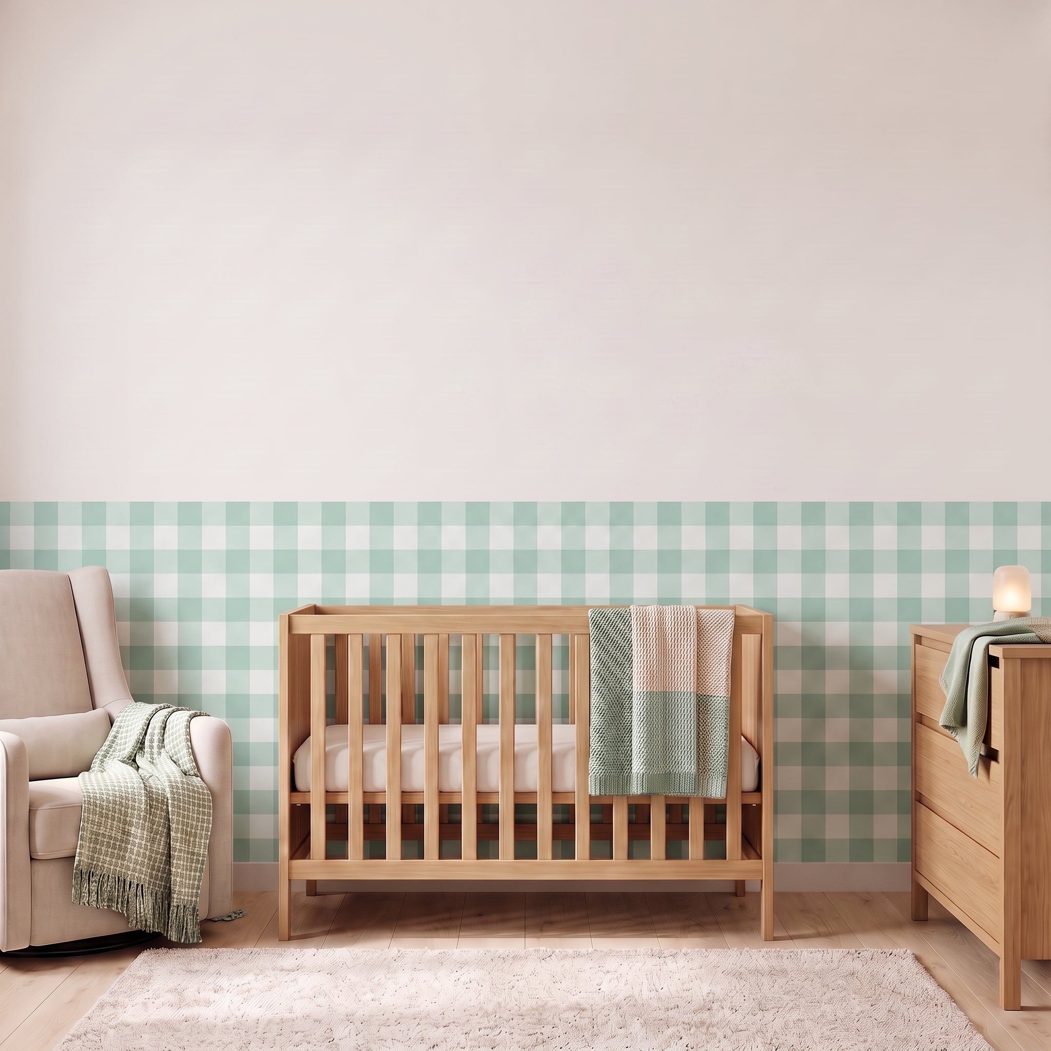 A styled nursery with seafoam green gingham check wallpaper across the lower half of the wall. The room has a light wood crib with white bedding and a seafoam and tan blanket, a cream armchair with a woven throw, a matching wood dresser with a lamp, and a soft rug on a light wood floor.