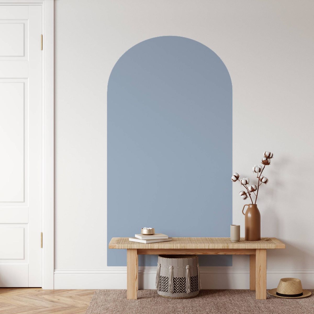 Arched blue mirror on a white wall with a wooden bench and decorative items.