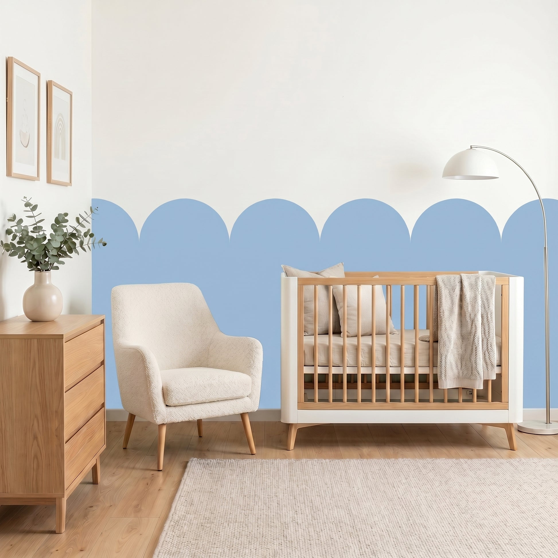 Nursery room with wooden crib, armchair, and dresser against a blue and white wall.