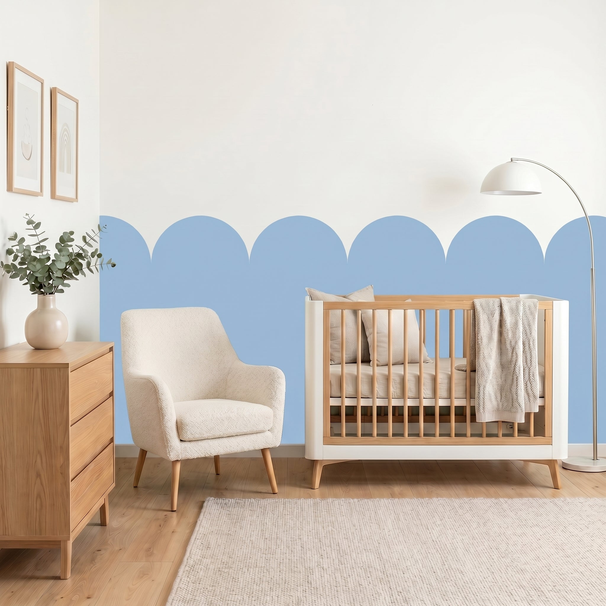 Nursery room with wooden crib, armchair, and dresser against a blue and white wall.