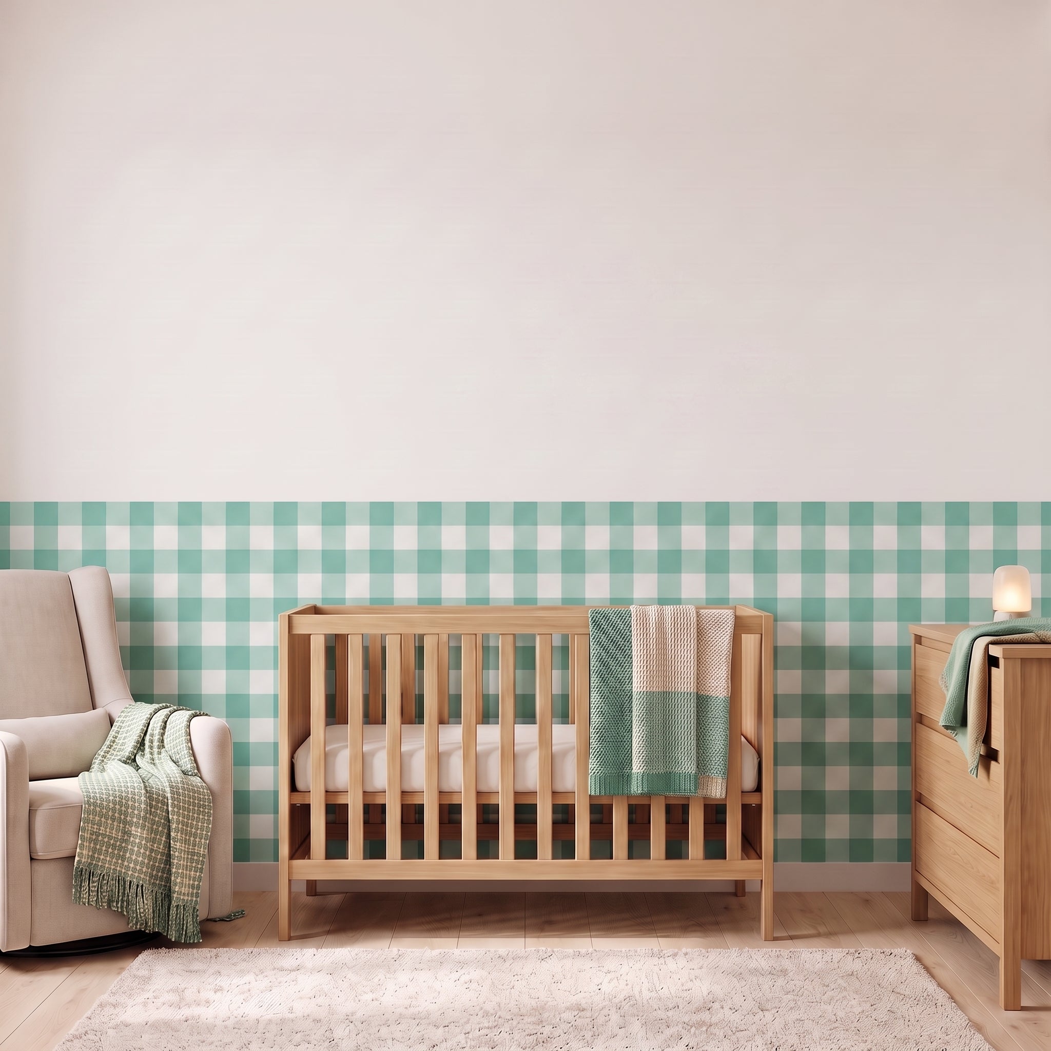 A styled nursery with soft teal gingham check wallpaper across the lower half of the wall. The room has a light wood crib with white bedding and a soft teal and tan blanket, a cream armchair with a woven throw, a matching wood dresser with a lamp, and a soft rug on a light wood floor.