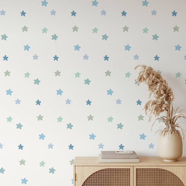 Blue and green star wall decals scattered across a white wall, styled above a light wood cabinet with a beige vase of dried grass and a book.