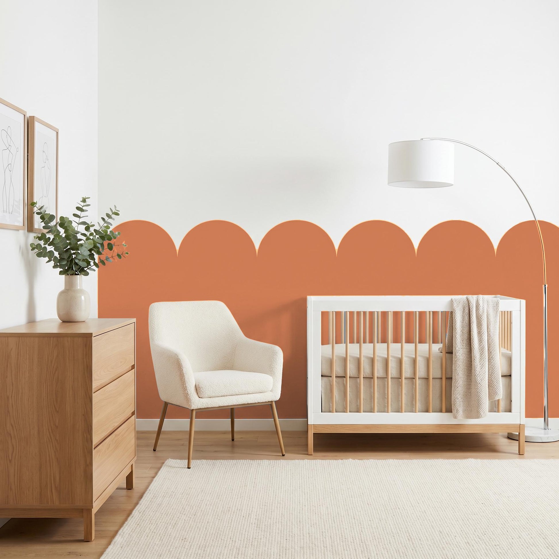 Nursery room with wooden crib, white chair, and dresser against an orange accent wall.