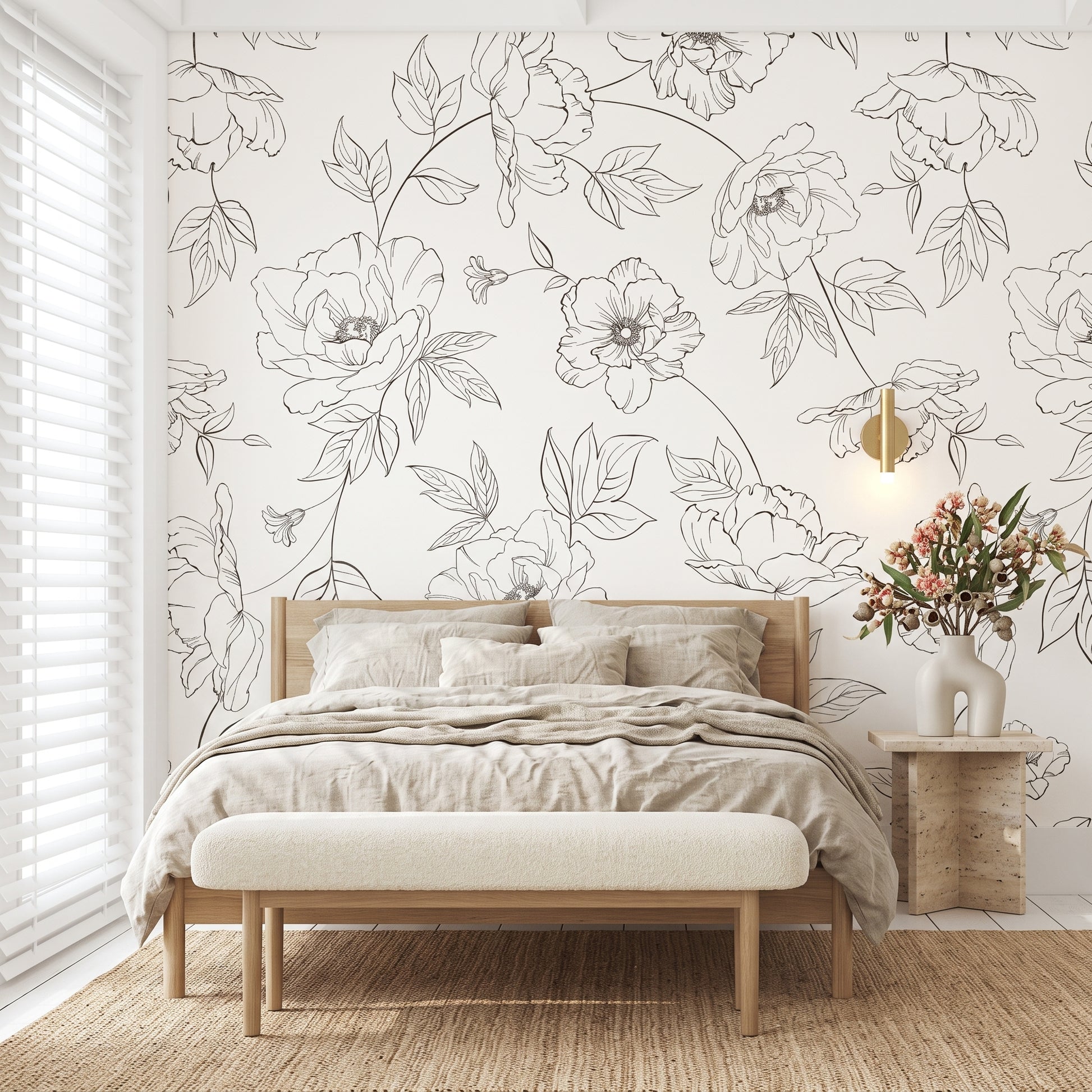 A styled bedroom featuring a white wallpaper with elegant black floral line art, a light wood bed with beige bedding, a matching upholstered bench, and a side table with flowers.