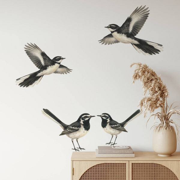 Three black-and-white bird wall decals displayed on a light wall above a wooden cabinet, with dried grass in a vase nearby.