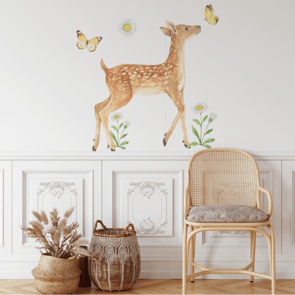 A wall decal set featuring a sleeping deer, standing deer, daisy stalks, daisy heads, and butterflies, placed above a chair and beside a basket.