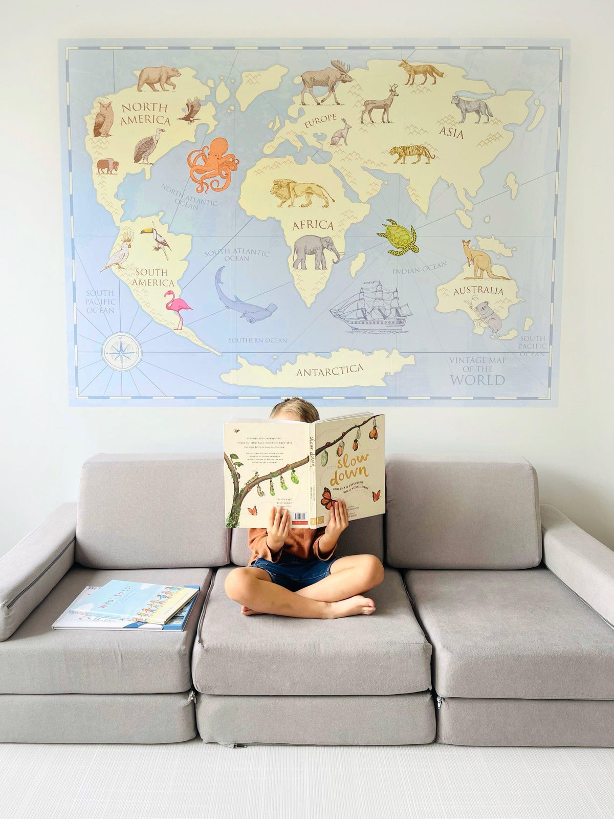 Child reading a book in front of the vintage world map wall decal