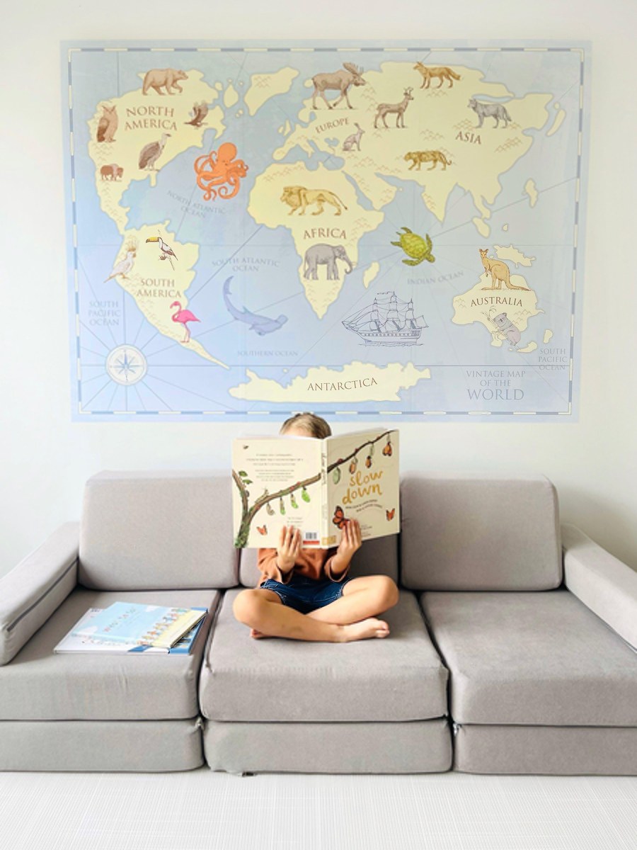 Child reading a book in front of the vintage world map wall decal