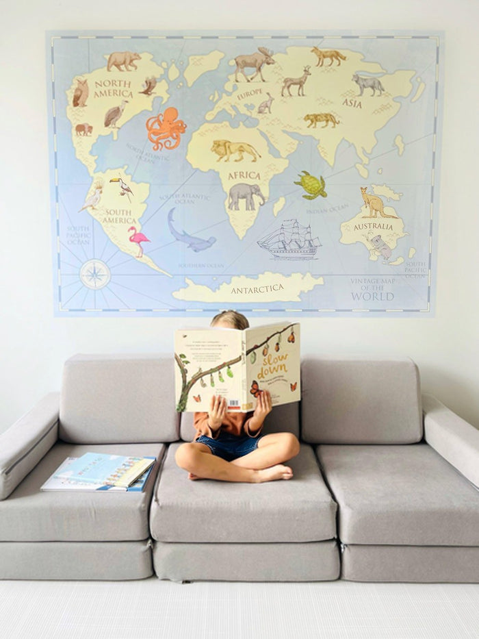 Child reading a book in front of the vintage world map wall decal