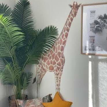 Tall giraffe wall decal beside a potted palm