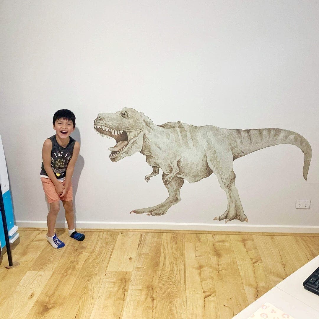 Child standing beside a large T-Rex dinosaur wall decal